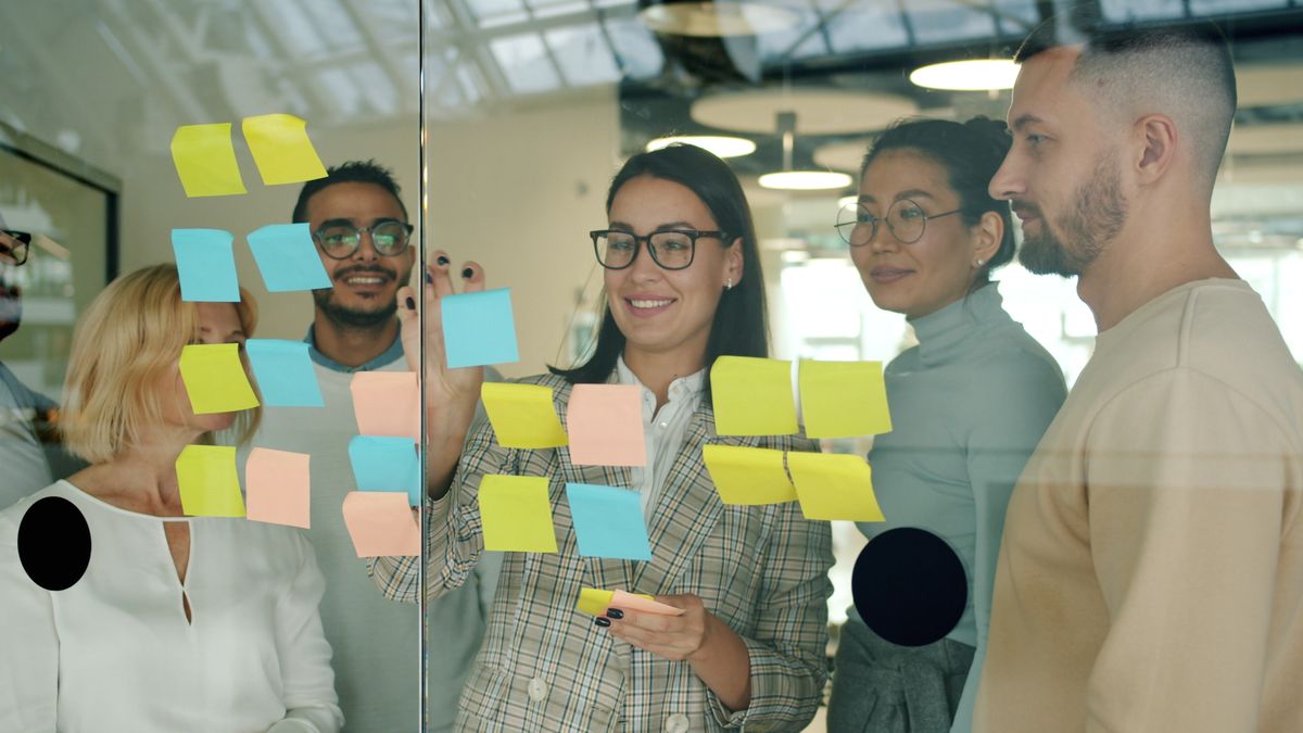 Équipe en séminaire de cohésion : cinq collègues échangent debout autour d’un mur de post-it
